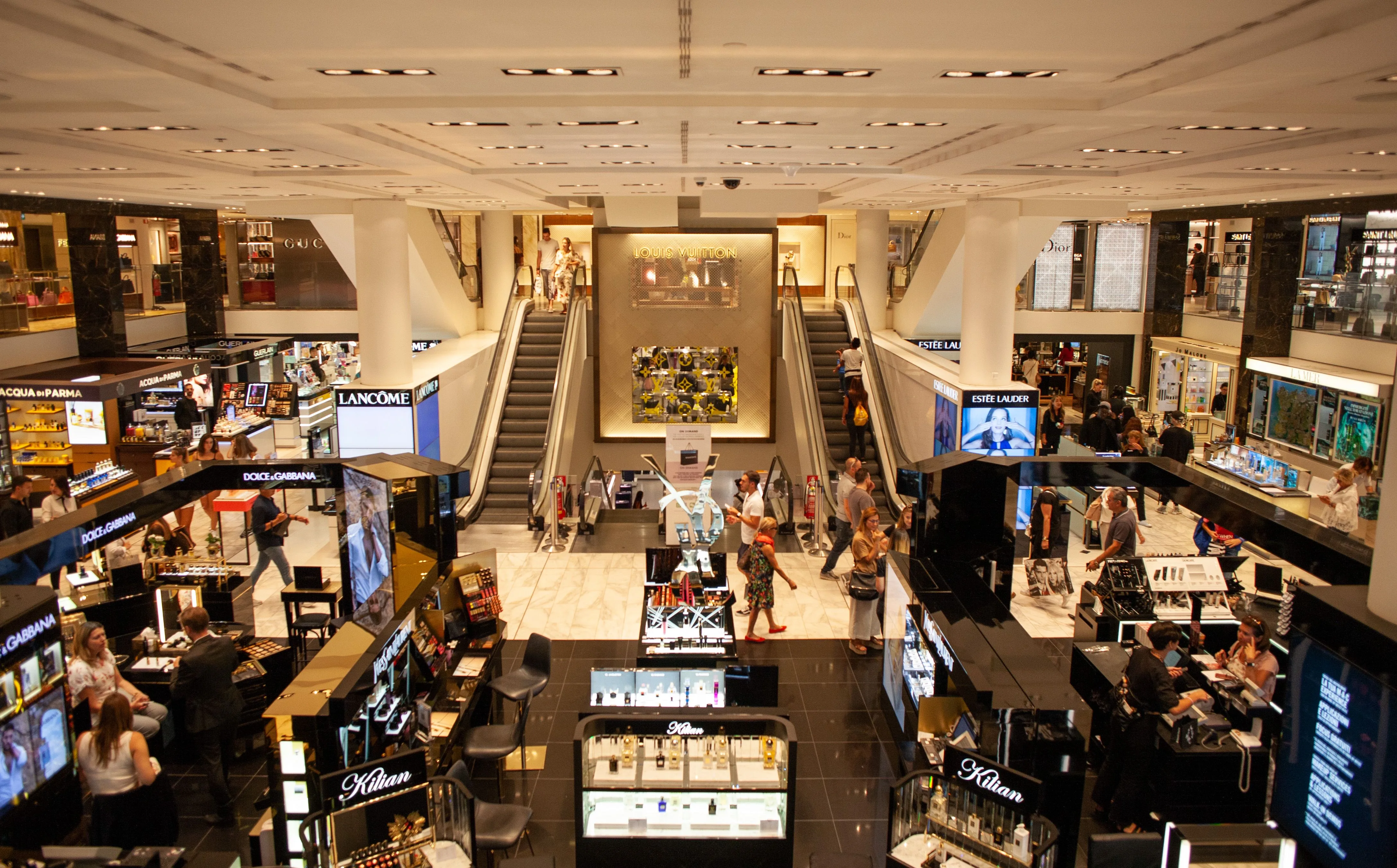 Interior de uma grande loja de retalho com vários balcões de marcas e clientes